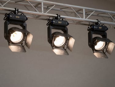 Detail shot of stage lighting fixtures mounted on a truss rig inside an event space, lights aimed at an empty stage, clean neutral background, bright studio-quality lighting