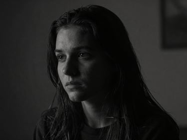Moody cinematic still from an independent film, high-contrast chiaroscuro lighting, deep shadows, desaturated monochrome tones, shallow depth of field.