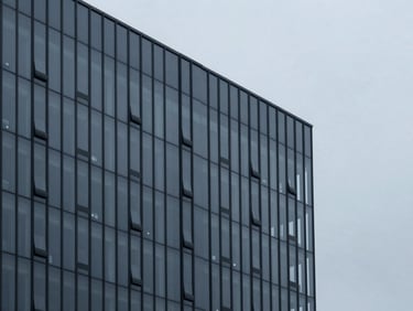 Minimalist editorial photography of a modern office building facade with glass reflections under overcast sky.