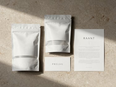 Overhead flat-lay of minimalist retail packaging and printed collateral on a warm taupe stone surface, natural side-lighting casting gentle shadows.