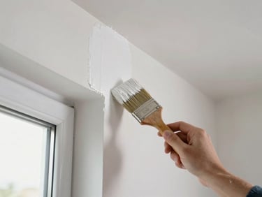 Close-up of a painter's brush applying bright white paint to an interior wall, natural window light, clean crisp edge where paint meets ceiling, documentary style