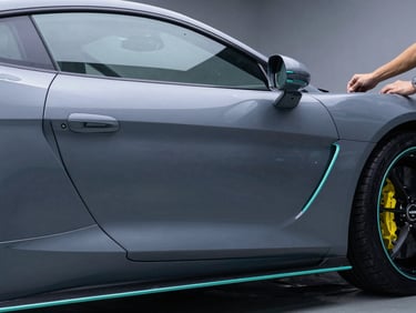 Sleek matte grey supercar side panel in a clean-room detailing studio, sharp neon teal highlights, professional installer hands visible at the edge, 35mm
