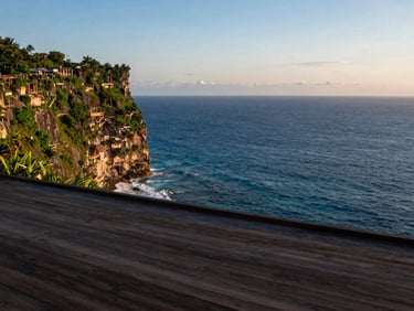 Minimalist wooden deck overlooking the Uluwatu cliffs at sunset, deep ocean blue tones, 35mm lens
