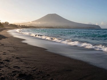 Empty black-sand beach in East Bali, slow-shutter water movement, misty volcanic horizon at dawn, 35mm lens