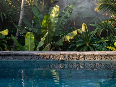 Tight editorial shot of a stone-carved pool edge in Ubud, lush tropical foliage reflection, morning mist, 35mm lens.
