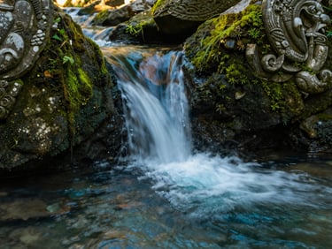 Slow-shutter water movement in a sacred mountain spring, mossy stone carvings, soft overcast light.