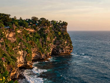 Wide environmental landscape of Uluwatu cliffs at sunset, deep blue ocean, golden hour light, 35mm lens.