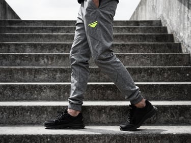 Low-angle shot of technical gray joggers on a model walking down concrete industrial stairs, high-contrast overcast daylight, sharp focus.