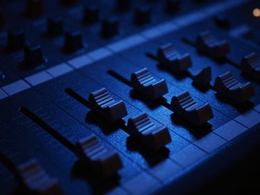 Close-up of analog mixing console faders under dramatic cobalt gel lighting, deep shadows, high-contrast