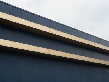 Abstract structural geometry of a light manufacturing facility, clean lines, soft overcast daylight, muted navy and champagne gold tones, sharp focus, 35mm lens
