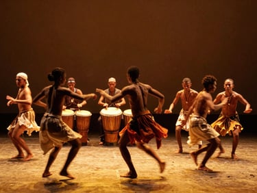 Wide environmental stage shot of dancers in dynamic motion blur, traditional atabaque drums visible in the background, warm golden lighting