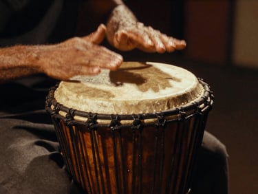 Close-up of expressive hands playing a traditional wooden atabaque drum, warm side-lighting, deep dramatic shadows, rich textures, 35mm film.