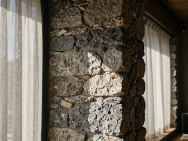 Close-up of raw stone walls and linen curtains inside a modern Bulgarian lodge, natural side light casting deep shadows