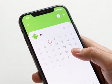 Close-up of an Android phone screen displaying a clean calendar app interface, hands interacting with the touch screen, bright studio light, vibrant green UI elements.
