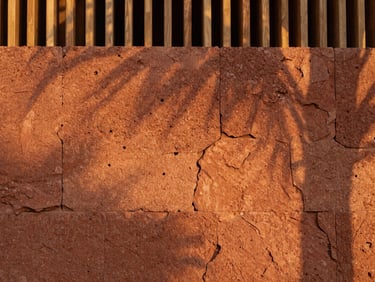 Close-up architectural detail of a porous laterite stone wall, warm terracotta tones, soft diffused golden-hour light filtering through a timber screen.