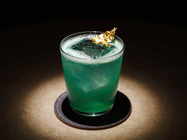 A vibrant emerald cocktail garnished with edible gold leaf, resting on a dark velvet coaster under a spotlight