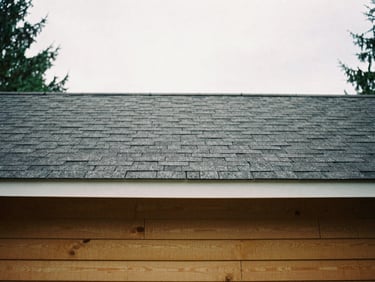 Close-up of clean dark gray architectural roof shingles and warm cedar siding under soft overcast daylight, 35mm film