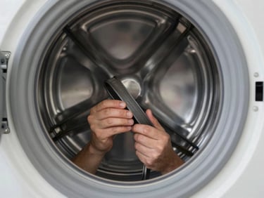 A technician inspecting the drum belt of an open front-load washing machine in a clean, bright laundry room