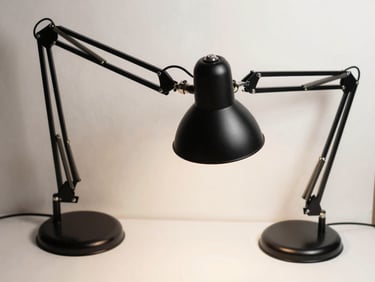 Strict top-down flat lay of a matte black articulated desk lamp on off-white paper.