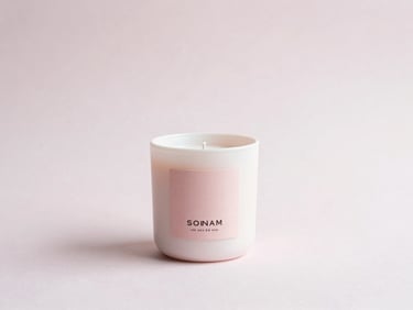 Small, centered product shot of a pale pink hand-poured candle in a white ceramic jar, with a custom label, soft natural light, minimalist composition.