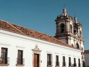 The white colonial facades and tiled roofs of Sucre, Chuquisaca, under a clear blue sky, clean architectural lines.