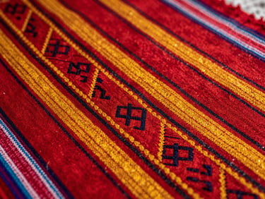 Close-up of vibrant traditional Bolivian aguayo textile, focusing on the intricate hand-woven geometric patterns and rich red and yellow threads under soft natural light