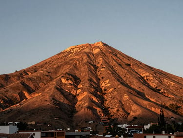 Cinematic shot of the Cerro Rico of Potosí at sunrise, warm golden light illuminating the historic terracotta-colored mountain.