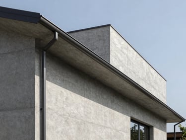 Wide architectural exterior shot of a modern minimalist concrete house under clear daylight, featuring a clean line of dark anodized aluminum gutter running perfectly along the roofline.