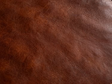Close-up of aged, rich brown leather with a developing patina, soft studio light highlighting texture, high-end editorial photography.