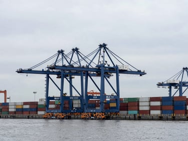 Wide-angle architectural view of a modern deep-water container terminal with massive blue gantry cranes under a cool overcast sky, desaturated navy tones, crisp industrial photography.