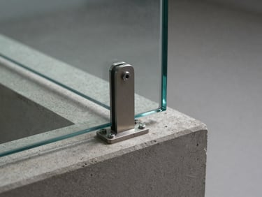 Tight shot of a frameless glass railing base channel bolted flush to a concrete stair nosing, structural clip hardware visible, soft studio light from above, no people, neutral gray background