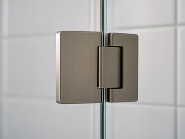 Extreme close-up of a frameless shower door hinge and glass edge, polished brushed-nickel hardware against clear tempered glass, soft diffused daylight from the left, white tile background, no people