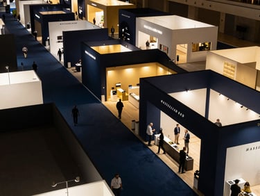 Overhead view of a bustling exhibition floor in Riyadh, showing clear pathways and strategic booth placement, high-contrast architectural lighting, deep navy and warm gold tones, sharp focus, Hasselblad 50mm