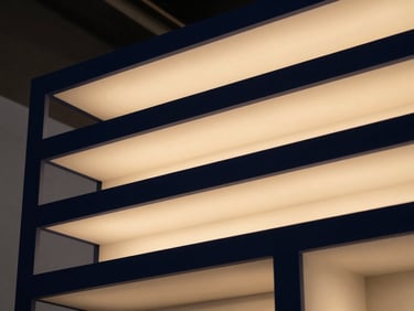 Close-up of sophisticated lighting fixtures illuminating a custom exhibition booth, highlighting premium materials and architectural lines, warm interior glow, deep navy and warm gold tones, sharp focus, Hasselblad 50mm