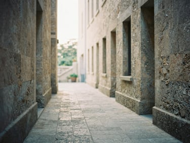 Weathered stone architecture, a quiet walking path leading into soft morning light, muted natural tones, shallow depth of field, 35mm film grain