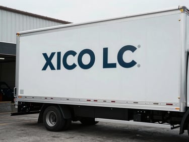 Exterior shot of a branded XICO LLC box truck, parked at a loading dock, secure cargo door visible, overcast daylight, cool desaturated tones.