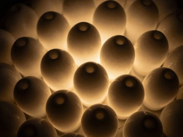 Macro close-up of hand-blown glass elements glowing with warm light, deep shadows, high contrast, intricate textures.
