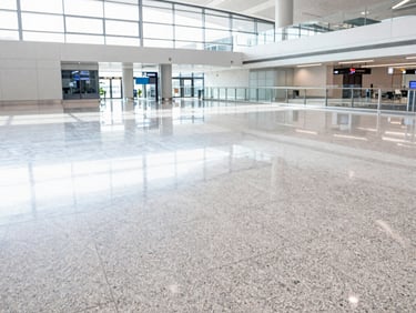 Wide-angle architectural shot of a bright, modern airport terminal floor, daylight reflecting off polished granite, 35mm