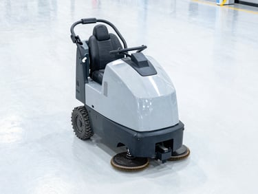Heavy-duty ride-on scrubber operating on a bright polished concrete floor in a modern warehouse, clean high-key daylight, 35mm