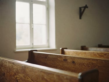 Soft morning window light filtering through wooden pews in a simple chapel, warm earth tones, shallow depth of field, 35mm film.