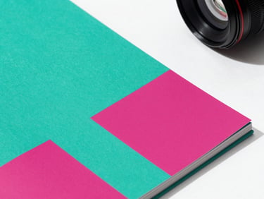 Close-up of a vibrant printed brand book with bold teal and orchid color blocks, sharp shadows, minimalist layout
