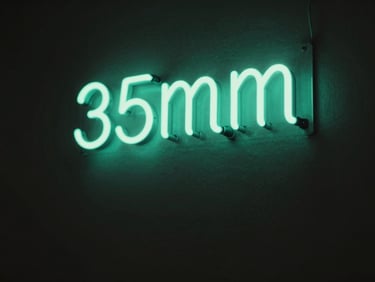 Low-key dramatic photo of a glowing sea-green neon sign on a dark charcoal wall, soft ambient light, shallow depth of field, 35mm