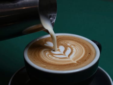 Close-up of latte art being poured into a dark ceramic cup, rich crema, moody low-key lighting, sea-green accents in the background, shallow depth of field, 35mm