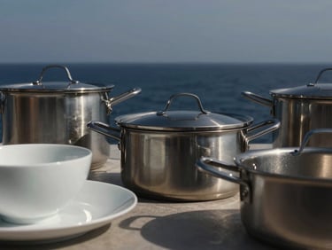 Kitchen & Dining. Minimalist close-up of durable stainless steel cookware and porcelain tableware, sharp architectural shadows