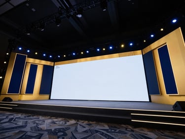 Wide-angle view of a corporate general session stage, deep navy lighting with sharp gold accents, large-scale LED walls displaying crisp graphics, professional atmosphere.