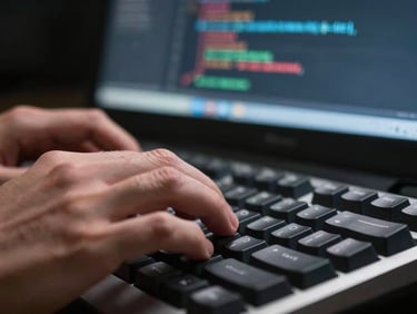 Extreme close-up of a developer's hands typing on a mechanical keyboard, code visible on a dark monitor screen behind, sharp focus on fingertips, studio lighting from the left