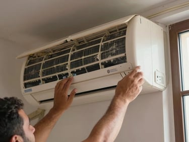 Close-up of a technician's hands removing the front panel of a wall-mounted air conditioning unit in a Moroccan apartment, natural daylight from a nearby window, dust on the filter visible, no faces, documentary framing