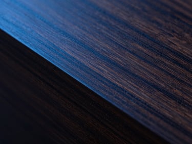 Macro shot of dark American walnut grain, perfectly sanded, meeting a clean edge, directional studio lighting, high contrast.