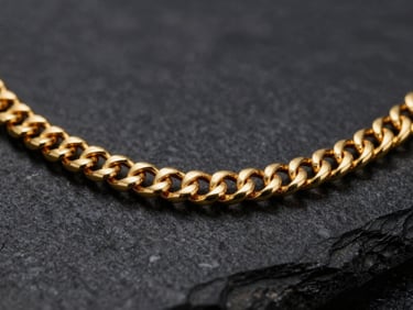 Macro shot of a thick hand-woven 22k gold chain resting on a dark stone surface, gleaming metallic highlights