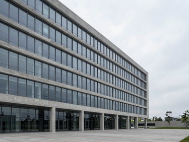 Wide panoramic shot of a minimalist glass and concrete corporate headquarters, soft overcast daylight, generous negative space on the right